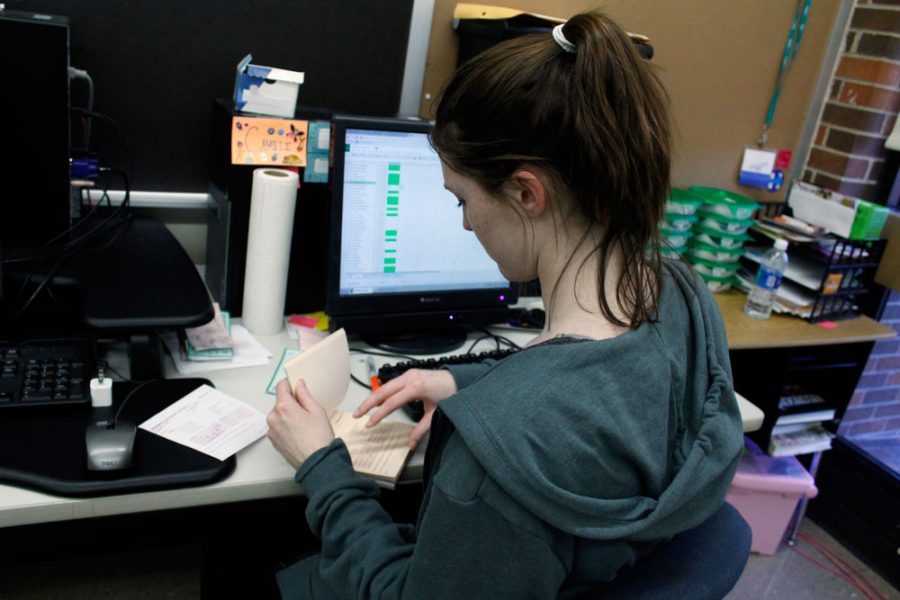 Senior Camille McManus, yearbook business manager, counts checks and book sale sheets at her desk.