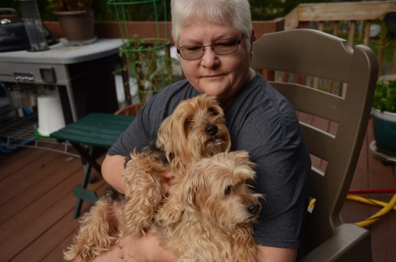 Dog lover Cheryl Spencer snuggles up with her dogs, Whiskey (left) and Brandy (right) on her back porch. After becoming a widow in 2015, Spencer found hope and comfort in her dogs as the three grieved their loss together. Photo by Allie Pigg. 
