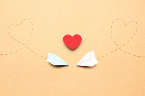 Creative valentines concept photo of two paper planes and a heart on brown background.