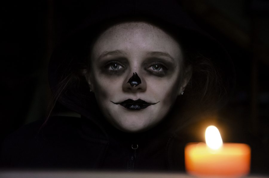 Junior Courtney Bach blends into the dark background where only her face is illluminated by the candle in the foreground. Her face is painted with makeup to mimic a skull. Photo by Sarah Mosteller.