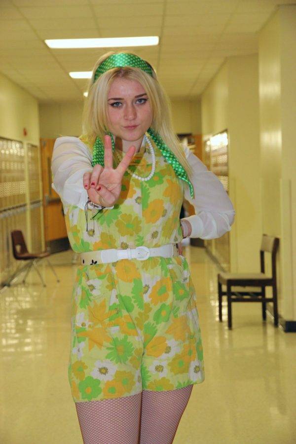Junior Nora Croom pouts and holds a peace sign on her way to class 3rd hour. Her flower-child 60s inspired outfit comes from the theater costume closet, as she is close with the costumer of the choir program. 