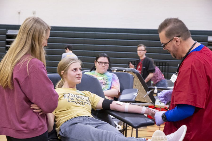 Junior Mackenzie Harvey looked away from the blood collection tube as she donated, staring instead at the gym ceiling. Standing next to her was her senior friend Ainsley Benson, supporting Harvey throughout the process. Photos by Sarah Mosteller.