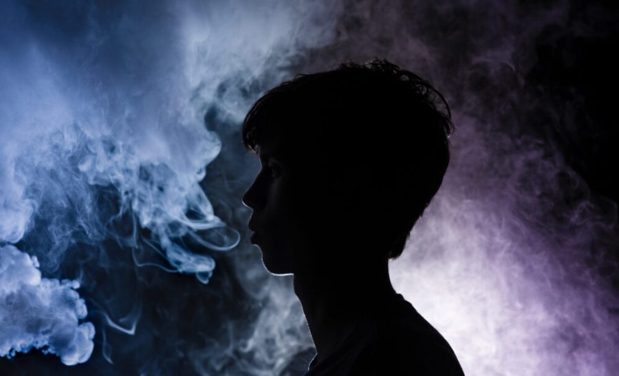 Junior Parker Boone exhales amidst a cloud of colored smoke, the outlines of his features barley visible in the dark. In December 2018, the Surgeon General issued an advisory on e-cigarette use among youth, declaring
the growing problem an epidemic. Featured image by Sophia Eaton.