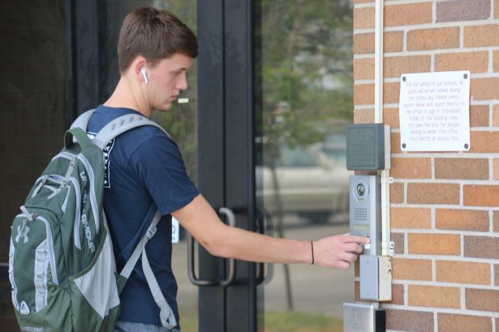 Senior Caleb Dunafon presses the buzzer to signal the office secretaries to unlock the doors at the north entrance on Sept. 20. While the office secretaries attend to other errands, students wait outside the north entrance. The north entrance doors are only open during passing periods, lunch, before school and after school. Photo by Sarah Mosteller