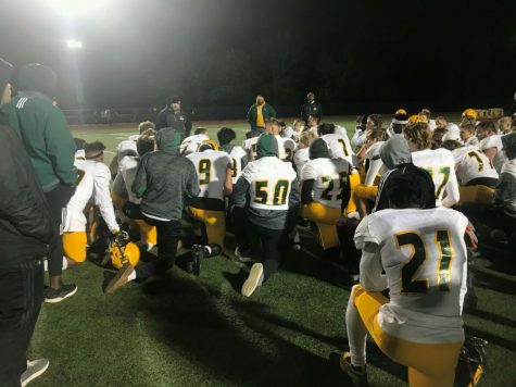 Junior cornerback and wide receiver Marquis McCaster (21) along with other RBHS players, kneel down in a huddle for one last post-game speech from Head Coach Van Vanatta. The Bruins fell to Blue Springs 17-10 on Nov. 1. Photo by Elliot Bachrach.