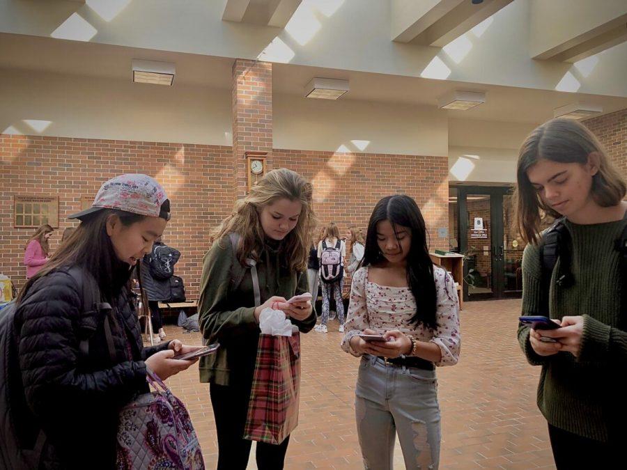 Four freshmen stand immersed in their phones. Photo by Inyoung Kim