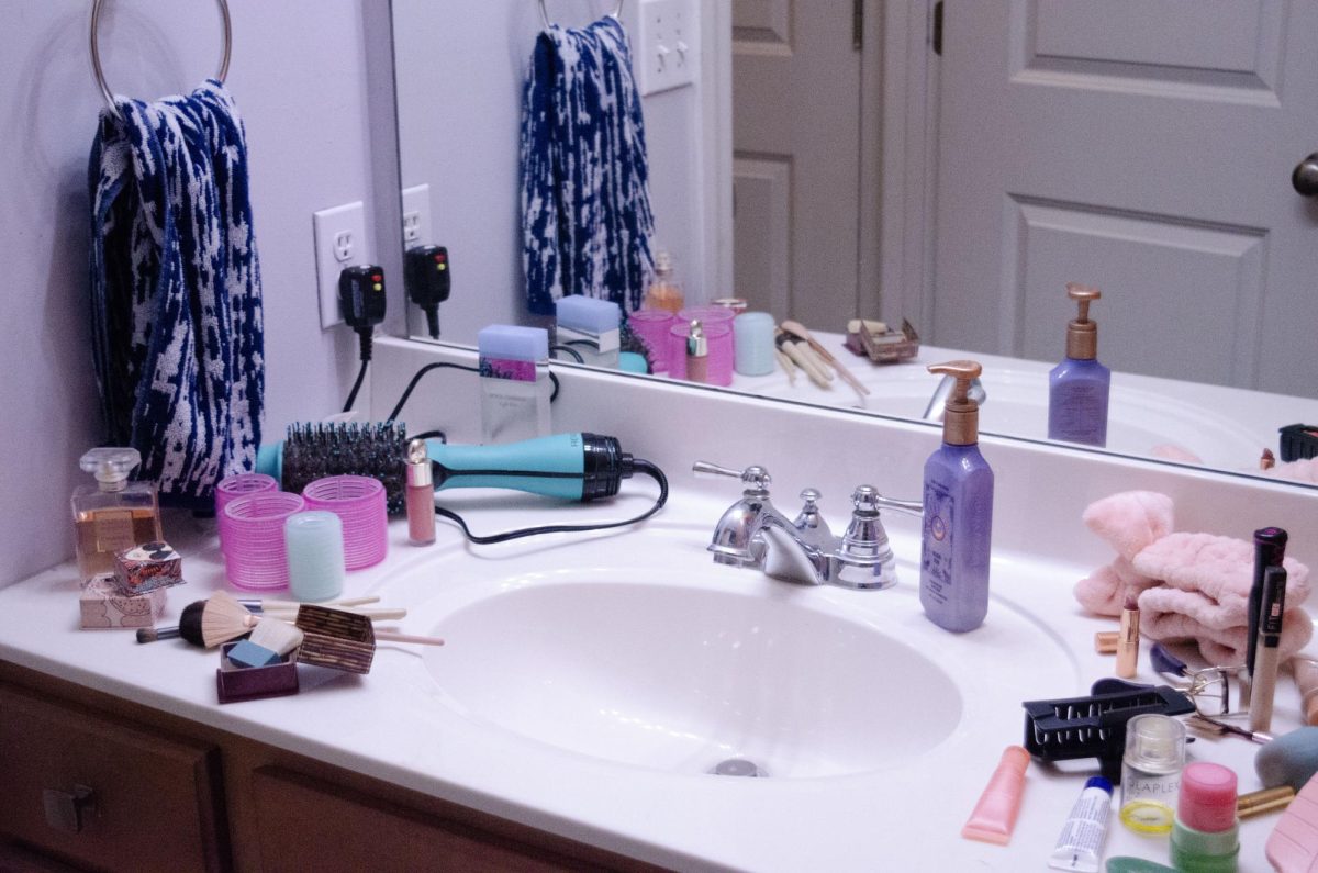 A bathroom sink cluttered with beauty products, including makeup, hair tools, and fragrances.  