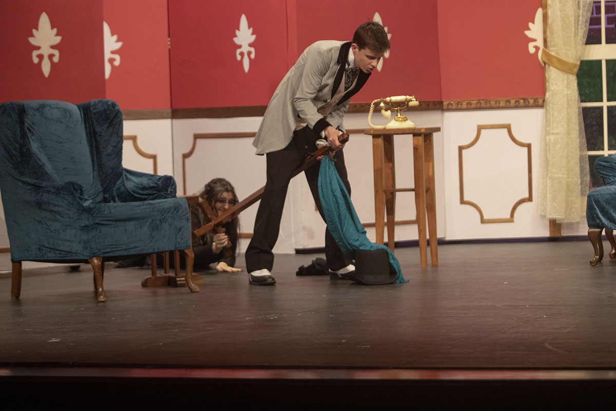 Billy Carewe, played by Harryson Schlegel (11), gets caught in a coat rack while trying to meet with his lover. Aggie Manville, played by Madison Torres (12), tries to drag the coat rack off stage. 