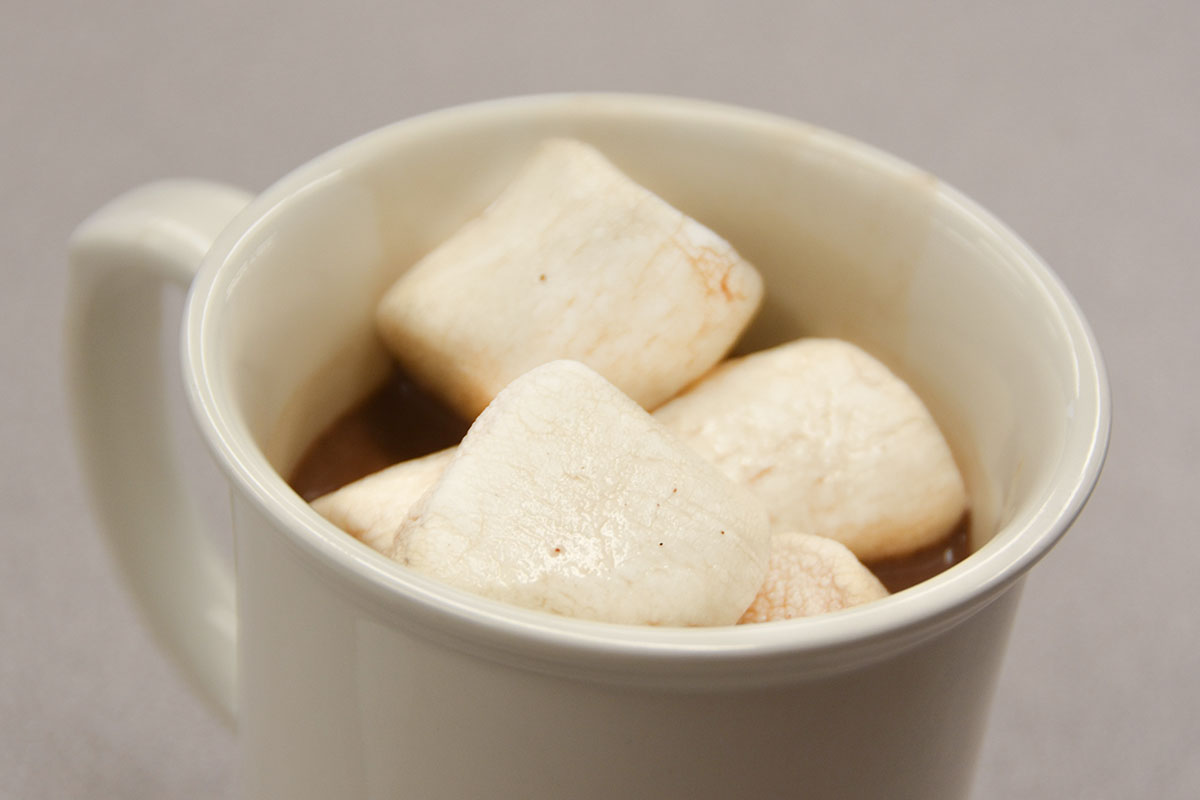 A delicious warm hot chocolate covered in marshmallows sits on the desk. 