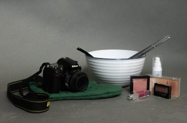 Still life photo of a camera, cooking supplies, and makeup essentials. These represent the careers of videography, the culinary arts, and cosmetology.