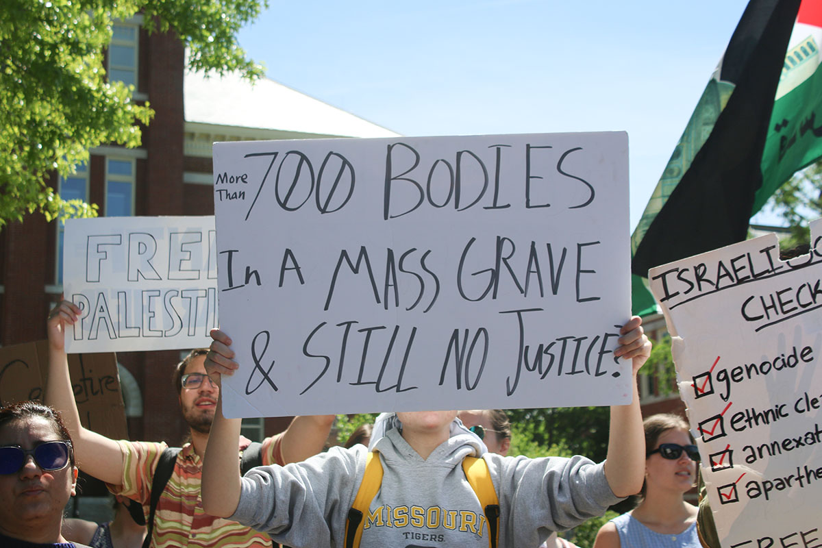 An MU student holds up a handmade sign which reads, More than 700 bodies in a mass grave & still no justice? Others wore keffiyehs and waved Palestinian flags.